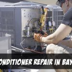 Air conditioner repair in Bay Head in white text on bottom of picture of man crouching in front of a condensor with a variety of tools