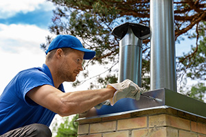 Manasquan chimney service professional at work on a roof wearing a blue shirt and hat and white work gloves