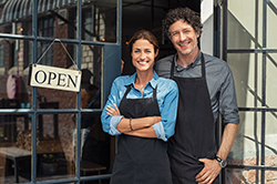 Shop owners in front of Lavallette store wearing black aprons posing by OPEN sign